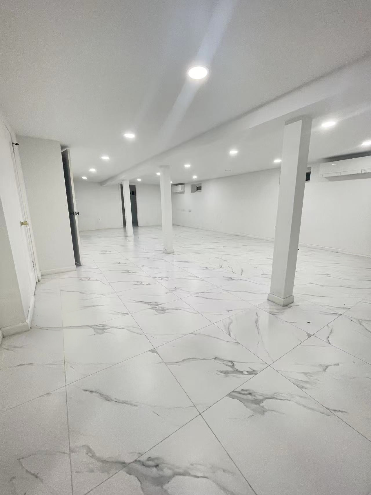 Massive fully finished basement with white marble-style porcelain tile in a District 26 Queens rental property.