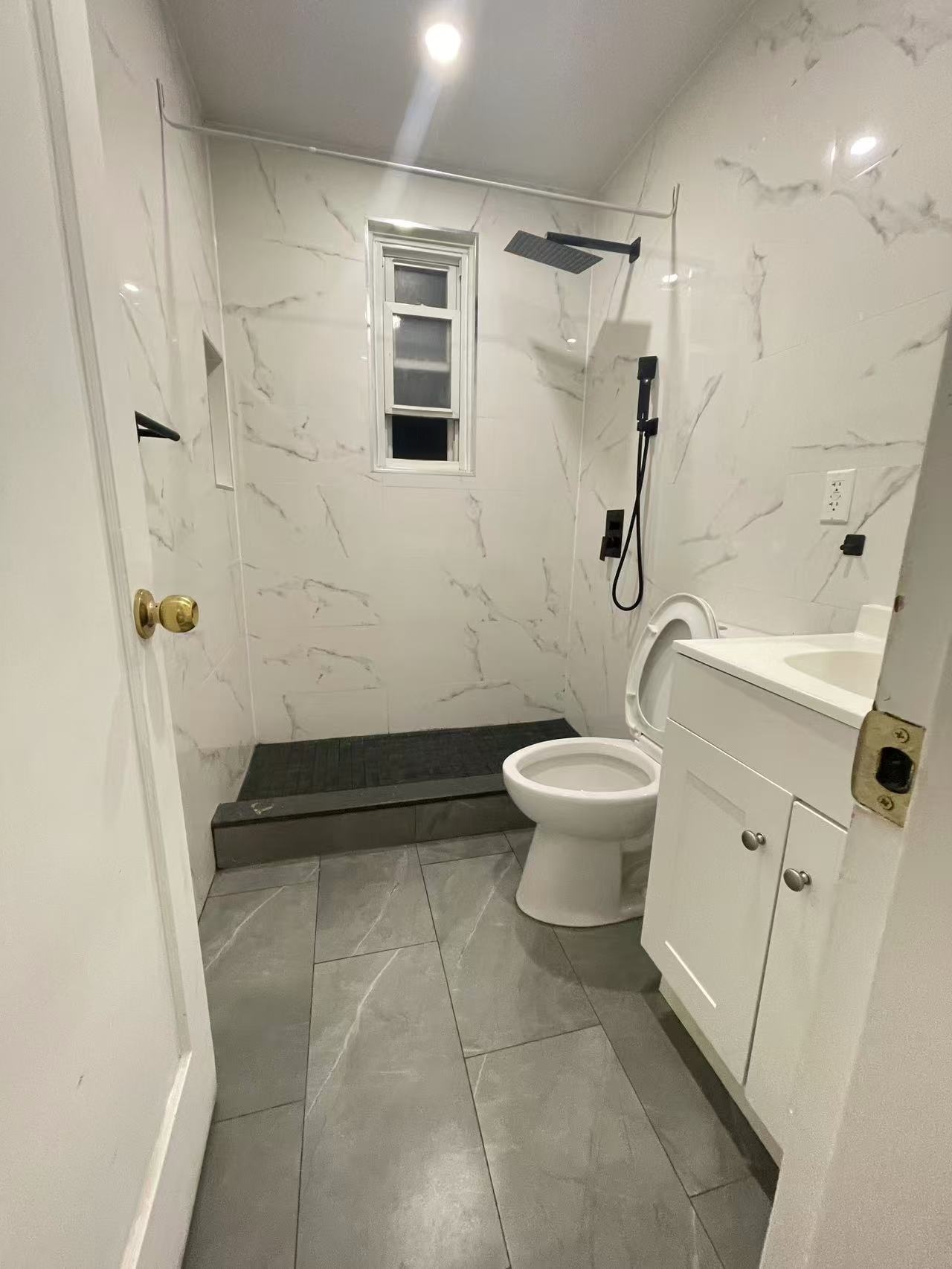 Modern spa bathroom with marble tile and matte black rain showerhead in a Fresh Meadows District 26 rental home.