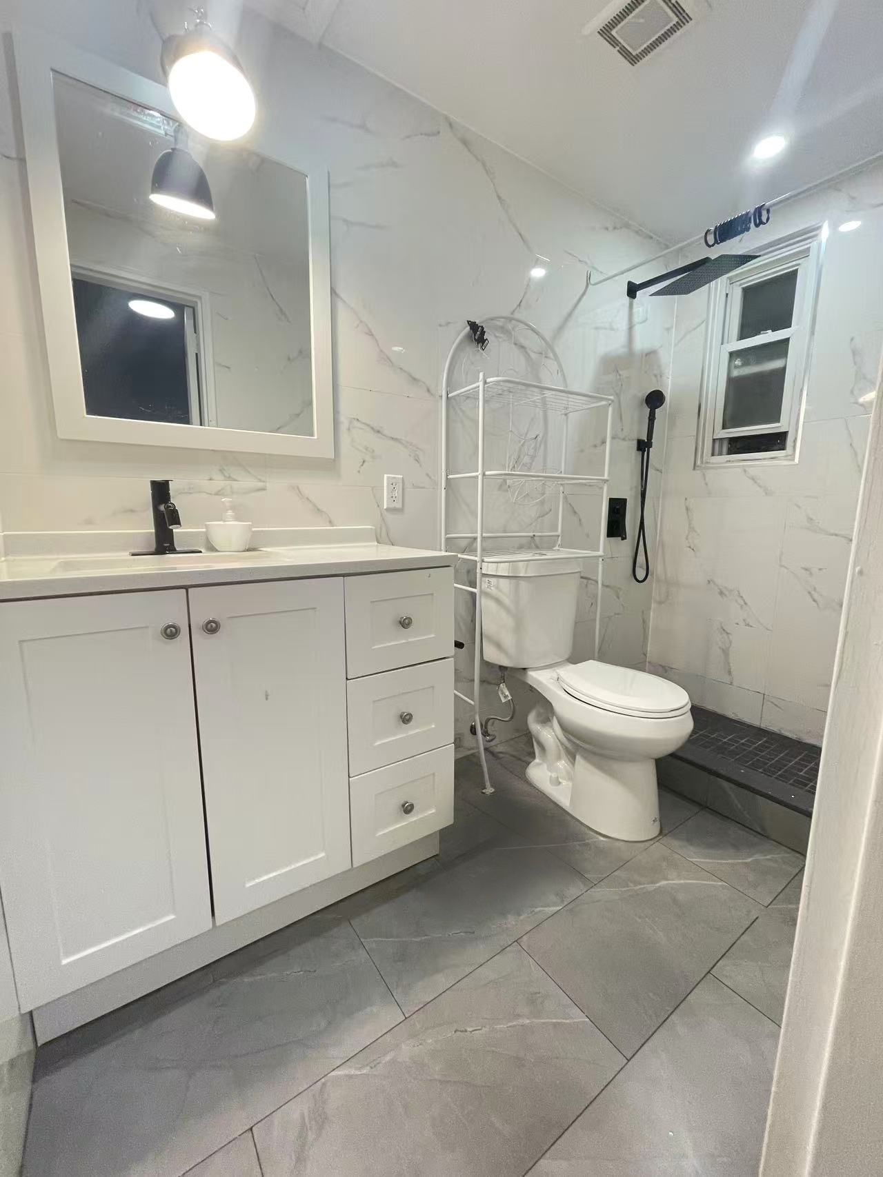 Updated full spa bathroom with white vanity and marble-veined walls in a Fresh Meadows rental house.