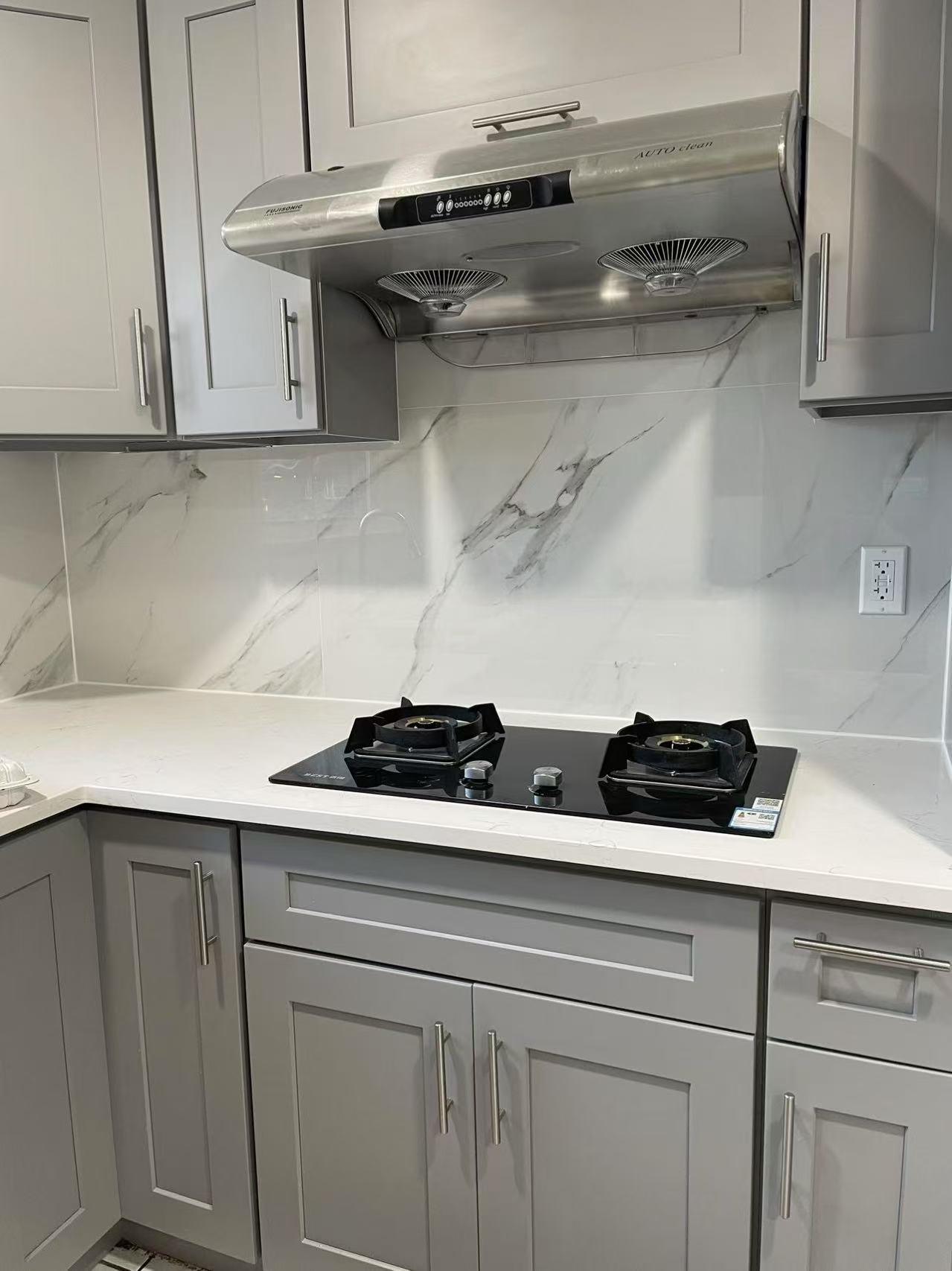 Renovated chef's kitchen with gas cooktop, grey cabinets, and marble backsplash in a Fresh Meadows house for rent.